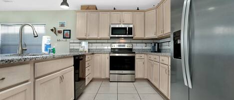 A modern kitchen with stainless steel appliances, light wood cabinets, and a granite countertop.