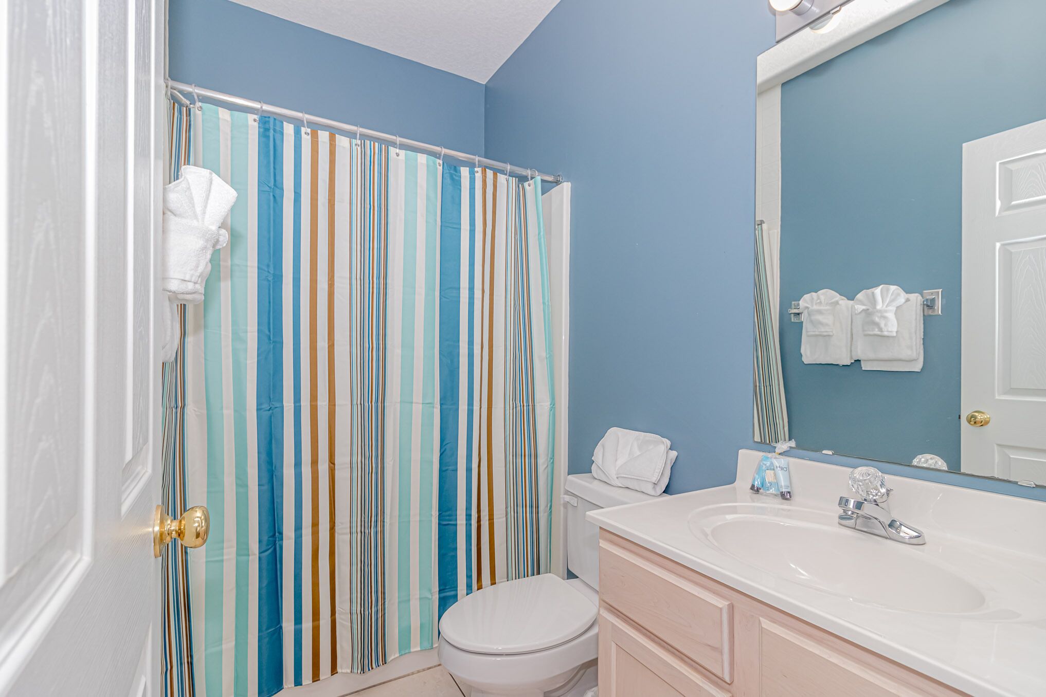 A bathroom with a striped shower curtain, a white toilet, a sink with a mirror, and towels hanging on the wall.