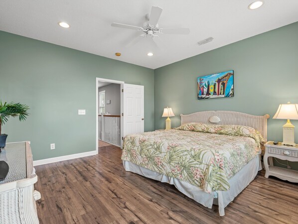 A bedroom with a bed, two bedside lamps, a ceiling fan, a painting, and a potted plant. - Walk to Beach Surfside House w/ Pool & 4 Bedrooms (Surfside Beach)