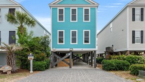 A two-story house with a raised foundation, a sign indicating it is a 'Seaside Inn', and a paved walkway leading to it. - Walk to Beach Surfside House w/ Pool & 4 Bedrooms (Surfside Beach)