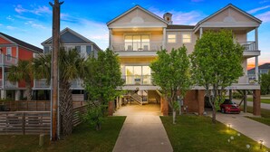 A two-story building with a balcony, a covered front porch, and a driveway leading to a parked car. - 5-Bedroom Home w/ Pool Near Surfside Beach (Surfside Beach)