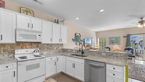 A kitchen with white cabinets, a microwave, stove, and dishwasher. There is a tiled backsplash and a rug on the floor. - 5-Bedroom Home w/ Pool Near Surfside Beach (Surfside Beach)