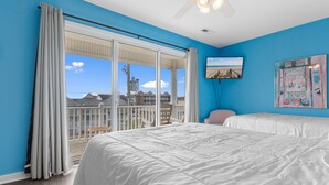 A bedroom with a large bed, a balcony with a view of buildings, a ceiling fan, and a painting on the wall. - 5-Bedroom Home w/ Pool Near Surfside Beach (Surfside Beach)