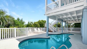 A swimming pool with a white deck, a covered upper level with a balcony, and a white fence surrounding the area. - 7-Bedroom Home w/ Private Pool & Beach Access (Garden City Beach)