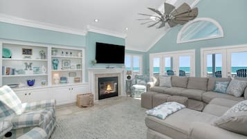 A living room with a fireplace, a television, and a view of the ocean.