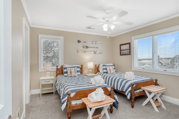 A bedroom with two beds, a ceiling fan, a window with blinds, and a nightstand with a lamp.