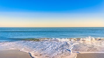 A beach with waves crashing onto the shore under a clear sky.