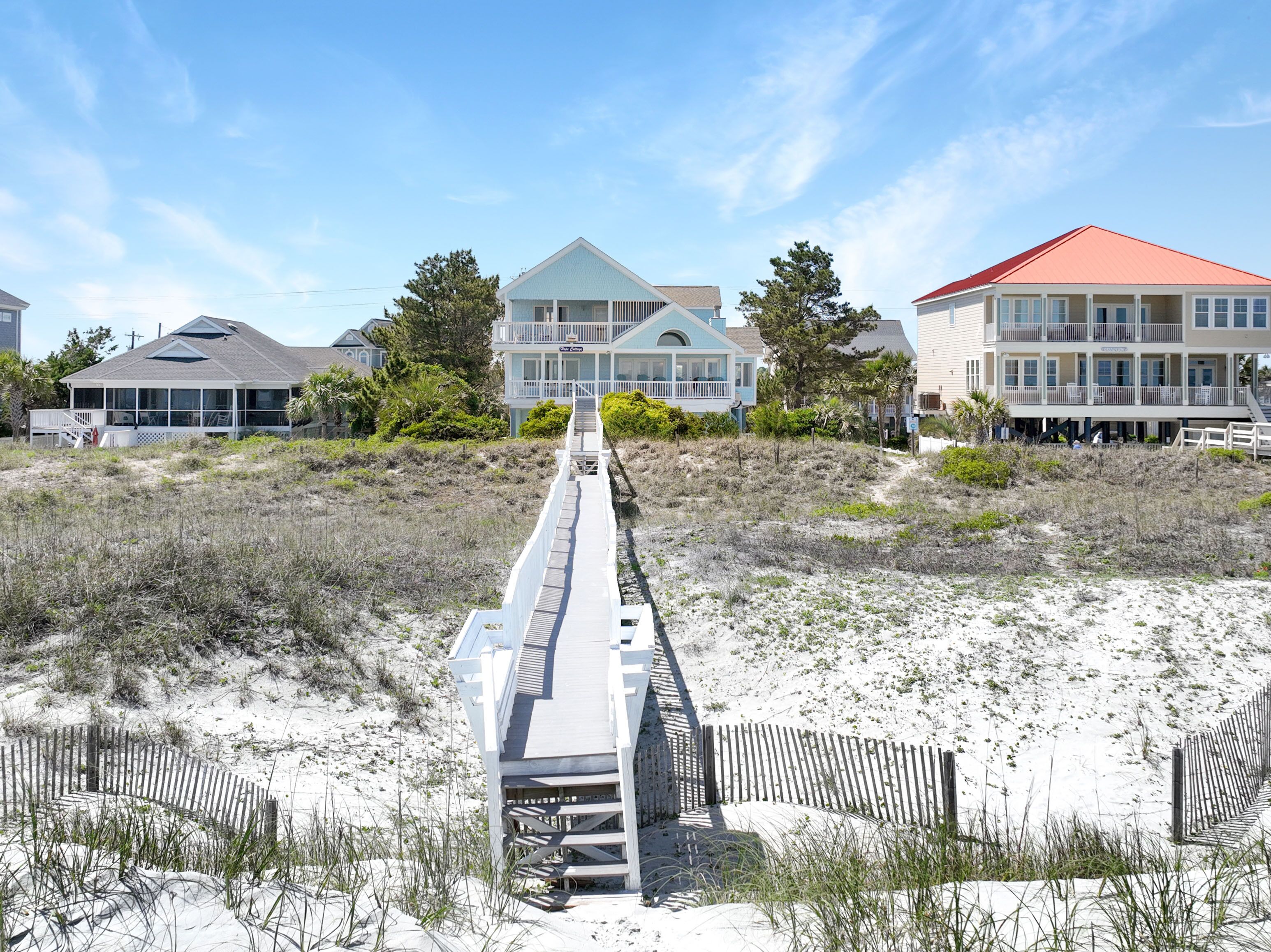 A beachfront property with a wooden boardwalk leading to a multi-story house with balconies.