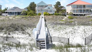 A beachfront property with a wooden boardwalk leading to a multi-story house with balconies. - 7-Bedroom Home w/ Private Pool & Beach Access (Garden City Beach)