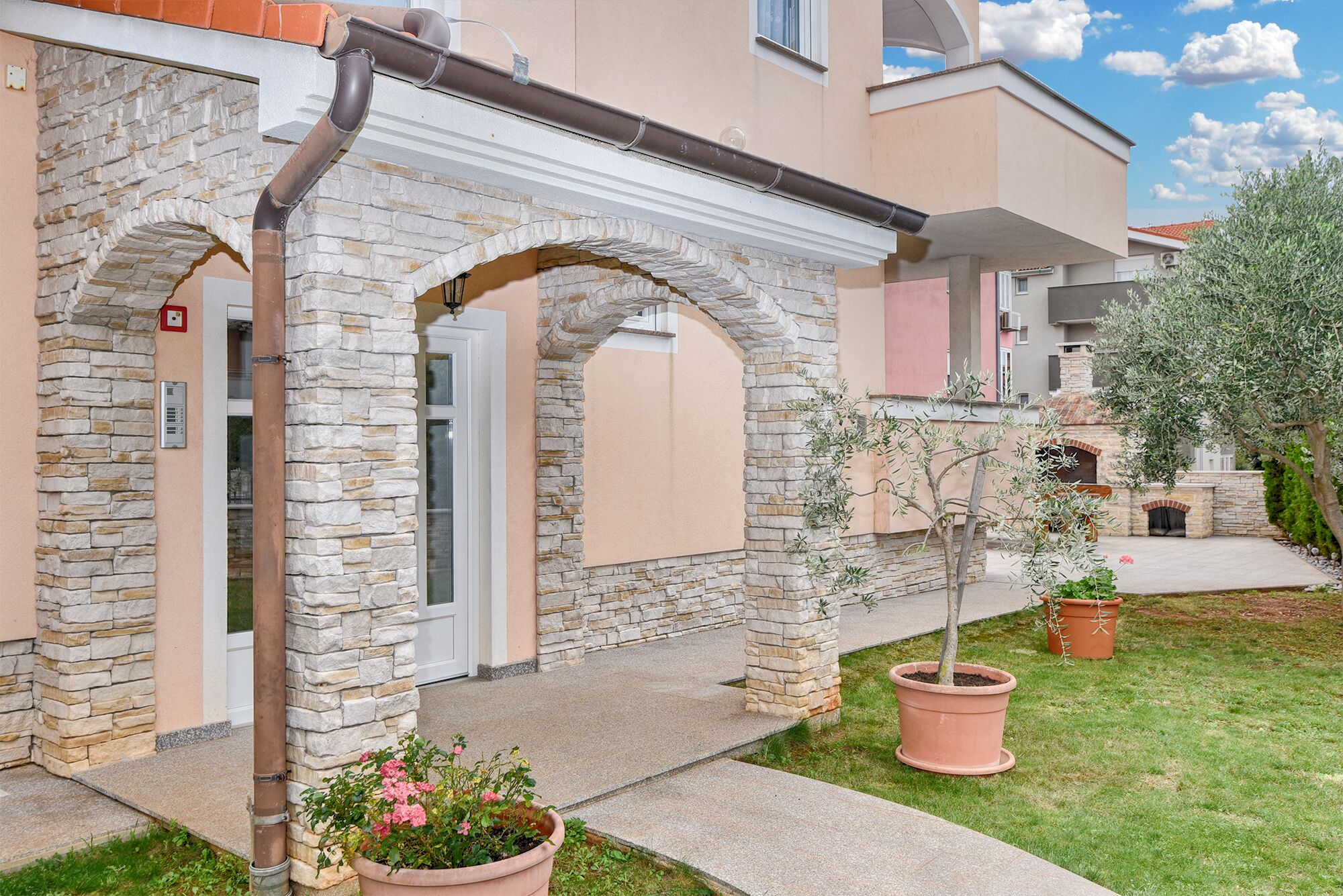 A building with stone arches, a small garden with potted plants, and a clear sky.