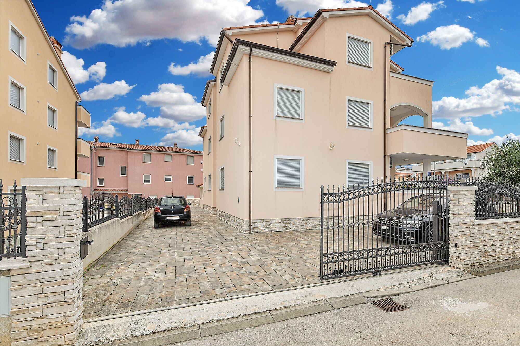 Una calle residencial con un camino de entrada pavimentado, un coche estacionado frente a una casa y un muro de piedra en un lateral.