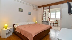 A bedroom with a wooden bed, two bedside lamps, a small bedside table, and a view of a dining area through an open door. - Apartment 405/917 (Istria - Medulin), 300m from the beach (Medulin)