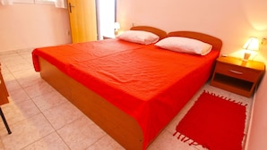 A single-bed room with a wooden frame, a red bedspread, a bedside table with a lamp, and a red rug.