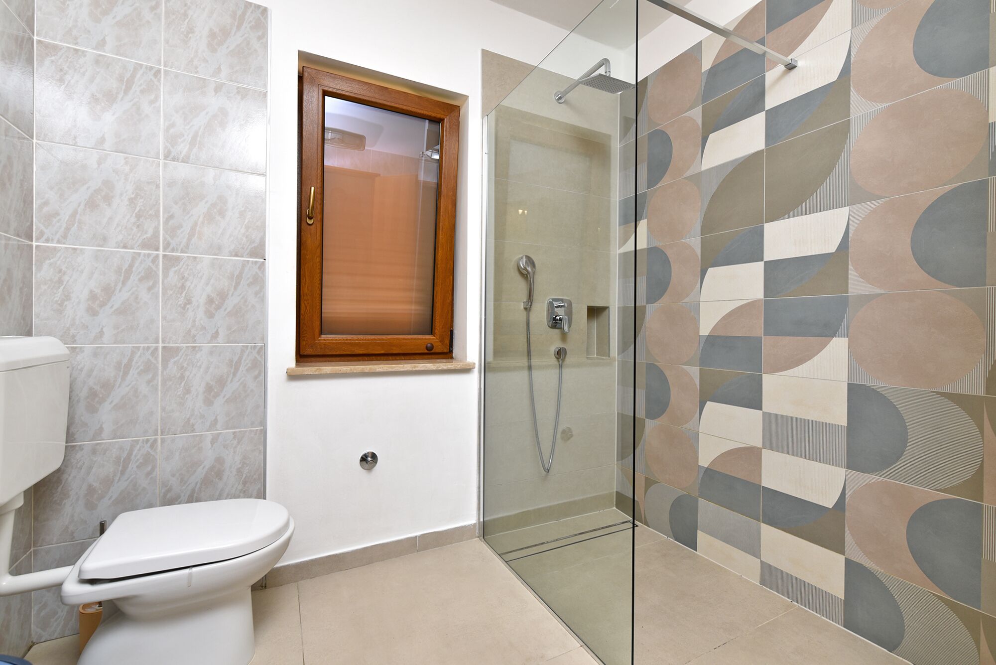 Een badkamer met toilet, douche met glazen deur en een behangen muur.