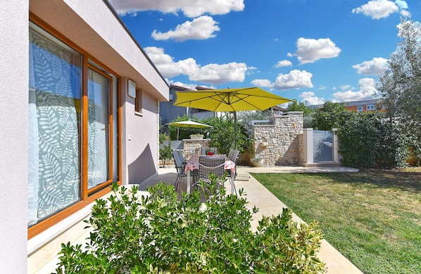 Relax in a serene outdoor space with a seating area, table, and umbrella, surrounded by lush greenery and a beautifully maintained lawn.