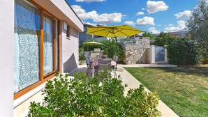 A patio with outdoor furniture and a yellow umbrella, a stone wall, and a grassy lawn.