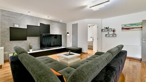 A modern living room with a large flat-screen TV, grey sofas, a coffee table, and a minimalist design.