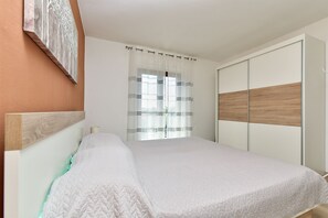Un dormitorio con cama, armario, ventana con cortinas y una obra de arte colgada en la pared.
