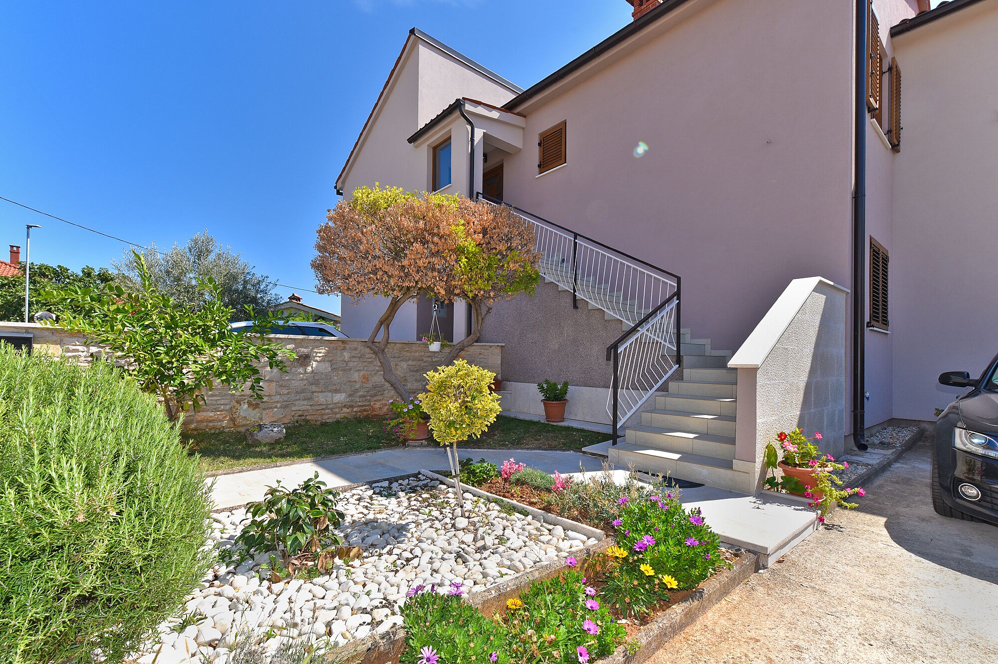 A residential building with a stone wall, a staircase, and a garden with various plants and flowers.