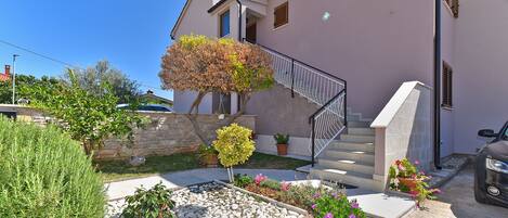 A residential building with a stone wall, a staircase, and a garden with various plants and flowers.