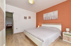 Un dormitorio con una cama, mesitas de noche, un cuadro y una puerta que da a otra habitación.