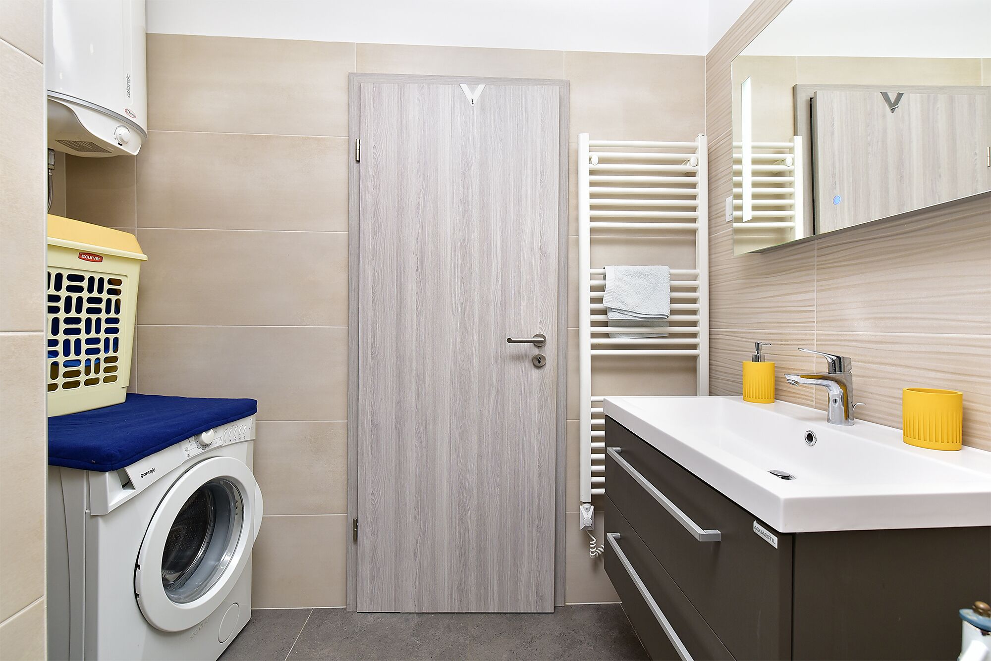 Een kleine badkamer met een wasmachine, een handdoekhouder en een wastafel met spiegel.
