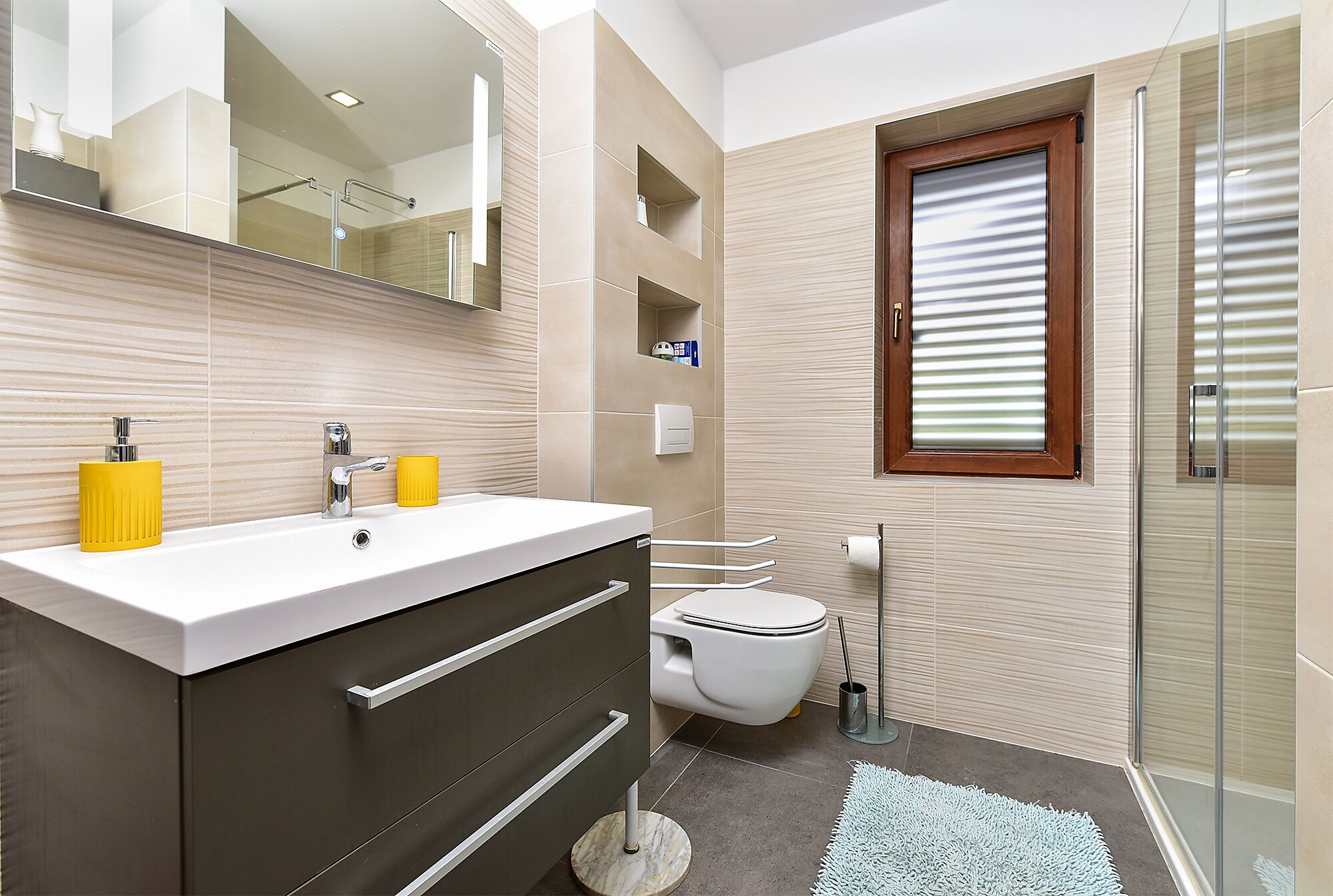 A modern bathroom with a large mirror, a white sink, a toilet, and a glass shower enclosure.
