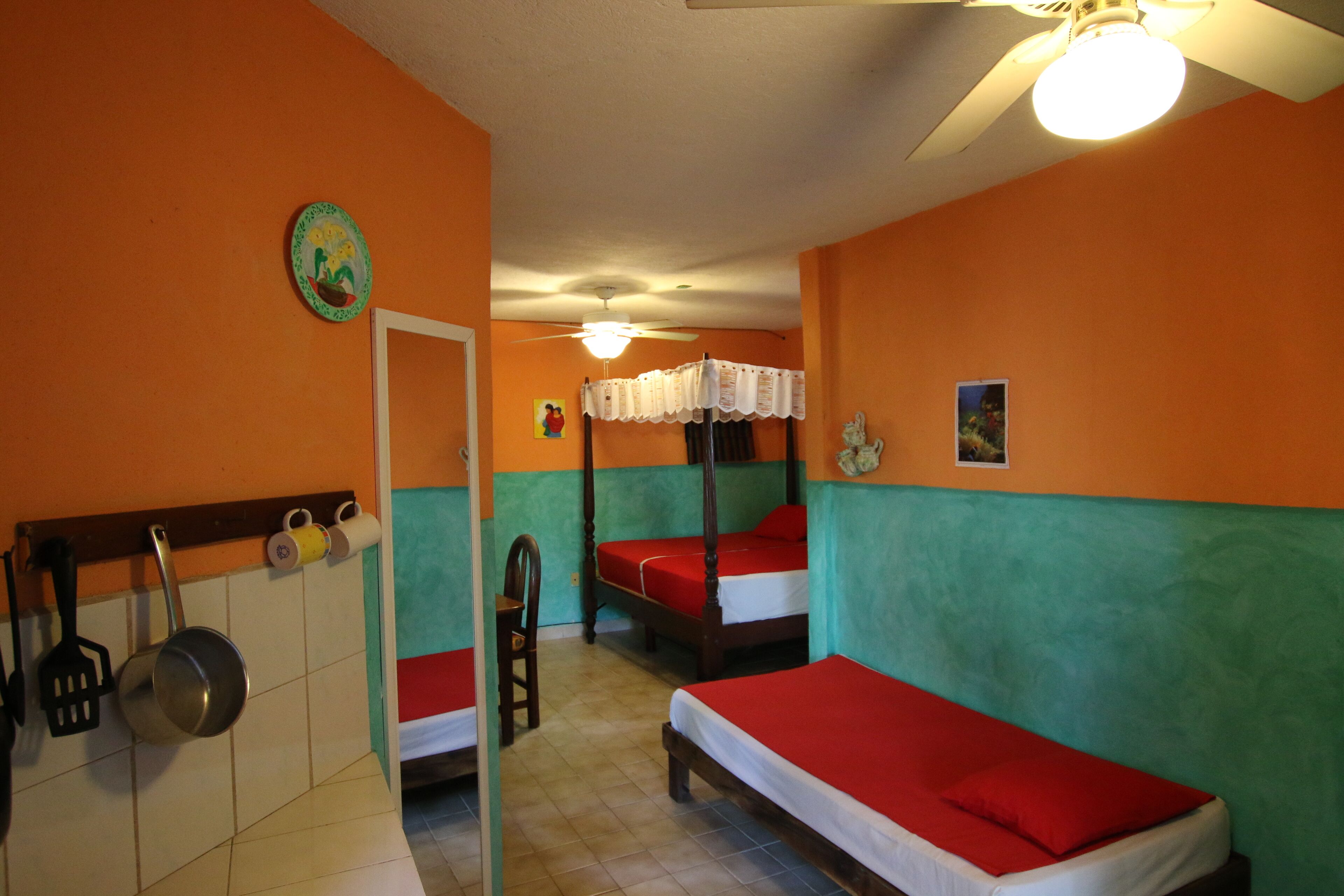 A room with two single beds, a ceiling fan, and a kitchenette with a stove and utensils.