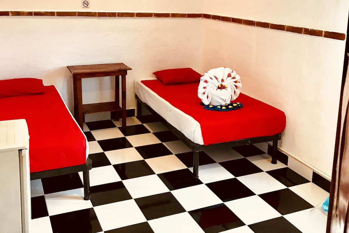 Ein Zimmer mit zwei Betten, einem kleinen Tisch, einem Deckenventilator und einem karierten Boden.