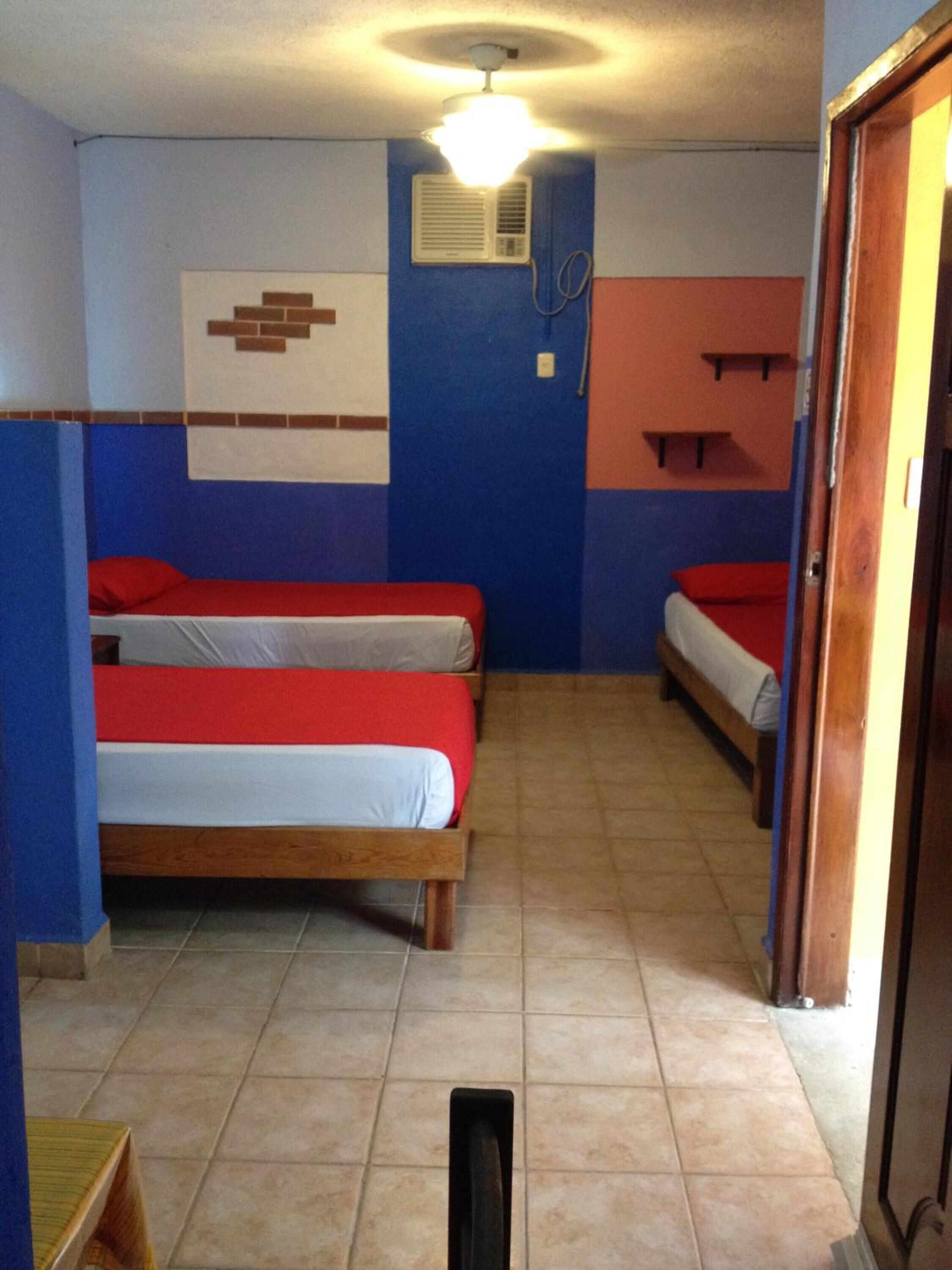 A small, compact room with two beds, a ceiling fan, and a wall-mounted air conditioning unit.