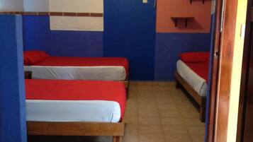 A small, compact room with two beds, a ceiling fan, and a wall-mounted air conditioning unit.