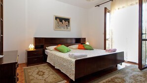 A bedroom with a wooden bed, a nightstand, a lamp, a painting on the wall, and a window with curtains.