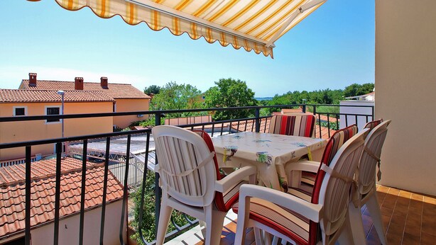 A balcony with a striped awning, outdoor furniture, and a view of buildings and greenery.