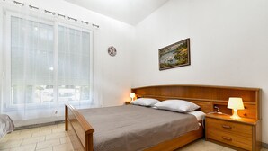 Une chambre à coucher avec un lit en bois, des lampes de chevet, une table de chevet, une fenêtre avec des rideaux légers et un tableau accroché au mur.