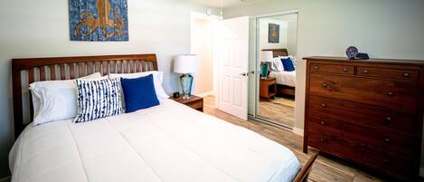 A bedroom with a wooden bed, a nightstand with a lamp, a dresser, and a ceiling fan.
