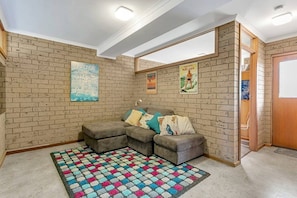 Une pièce avec un mur en briques, un canapé d’angle, un tapis coloré et deux affiches.