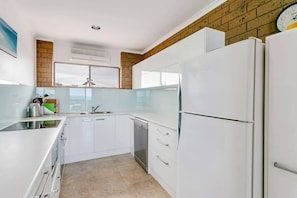 A modern kitchen with white cabinets, a stainless steel dishwasher, and a large refrigerator.