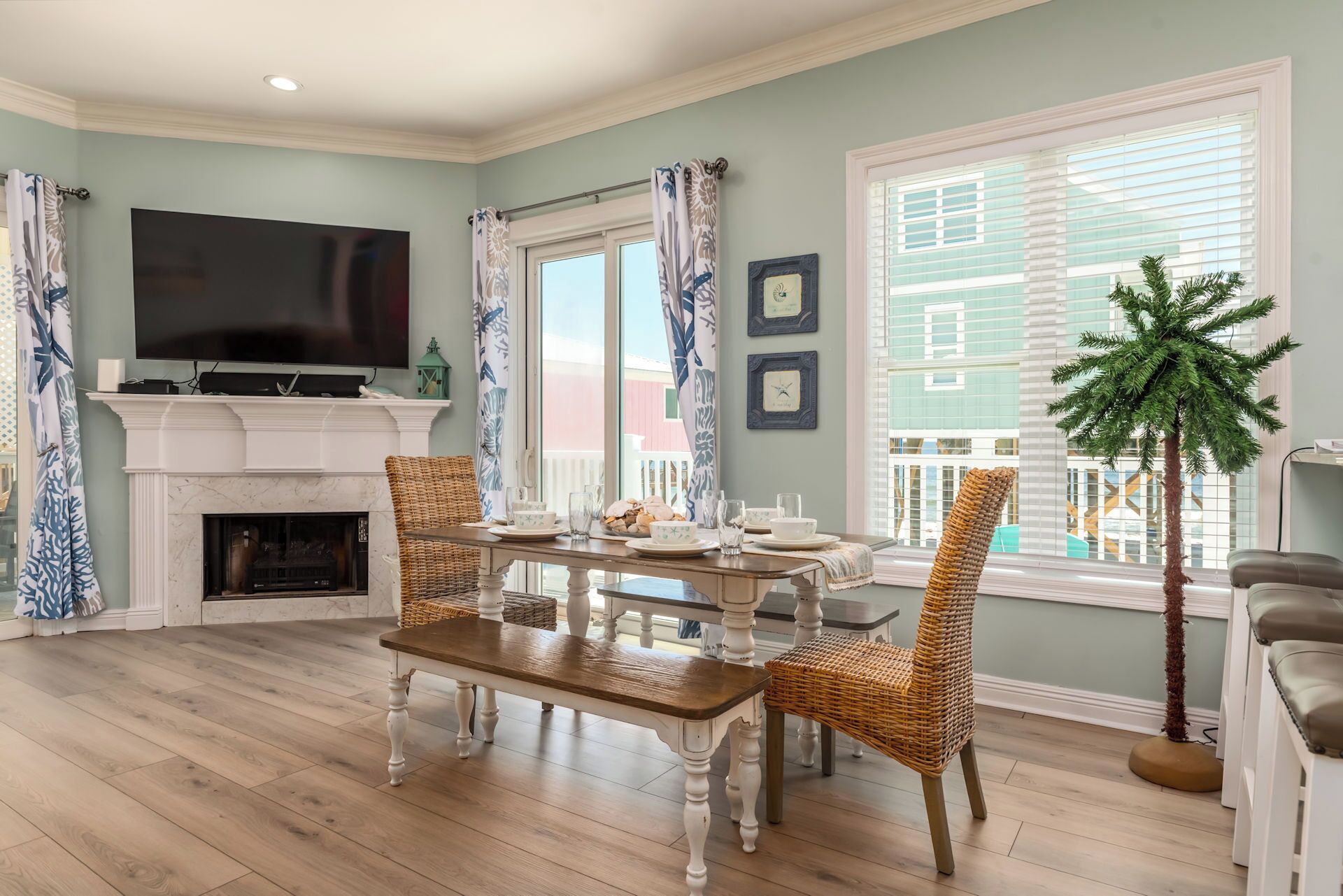 A living room with a fireplace, a television, a dining table with chairs, and a large window with blinds.