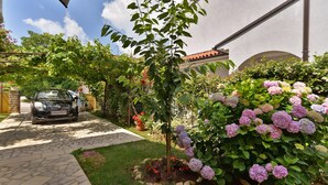 A garden with a car parked on a paved path, surrounded by lush greenery and flowering plants. - Apartment 436/1001 (Istria - Valbandon), 750m from the beach (Valbandon)