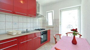 A compact kitchen with red cabinets, a gas stove, and a built-in oven. There's a window with a view of the outside, and a table with a vase of flowers. - Apartment 436/1001 (Istria - Valbandon), 750m from the beach (Valbandon)
