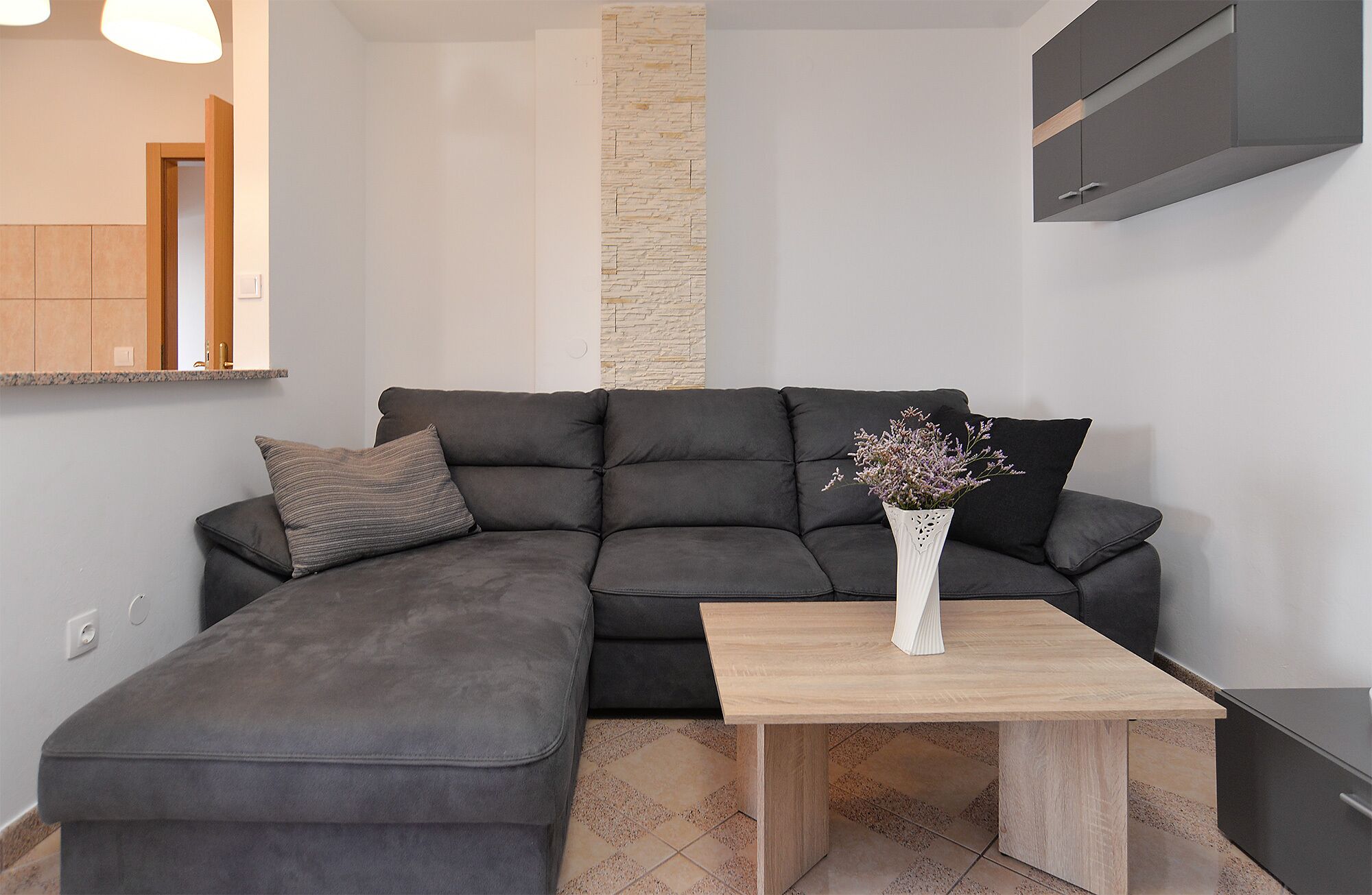 Ein modernes Wohnzimmer mit einem Ecksofa, einem Holztisch und einer Vase mit Blumen.