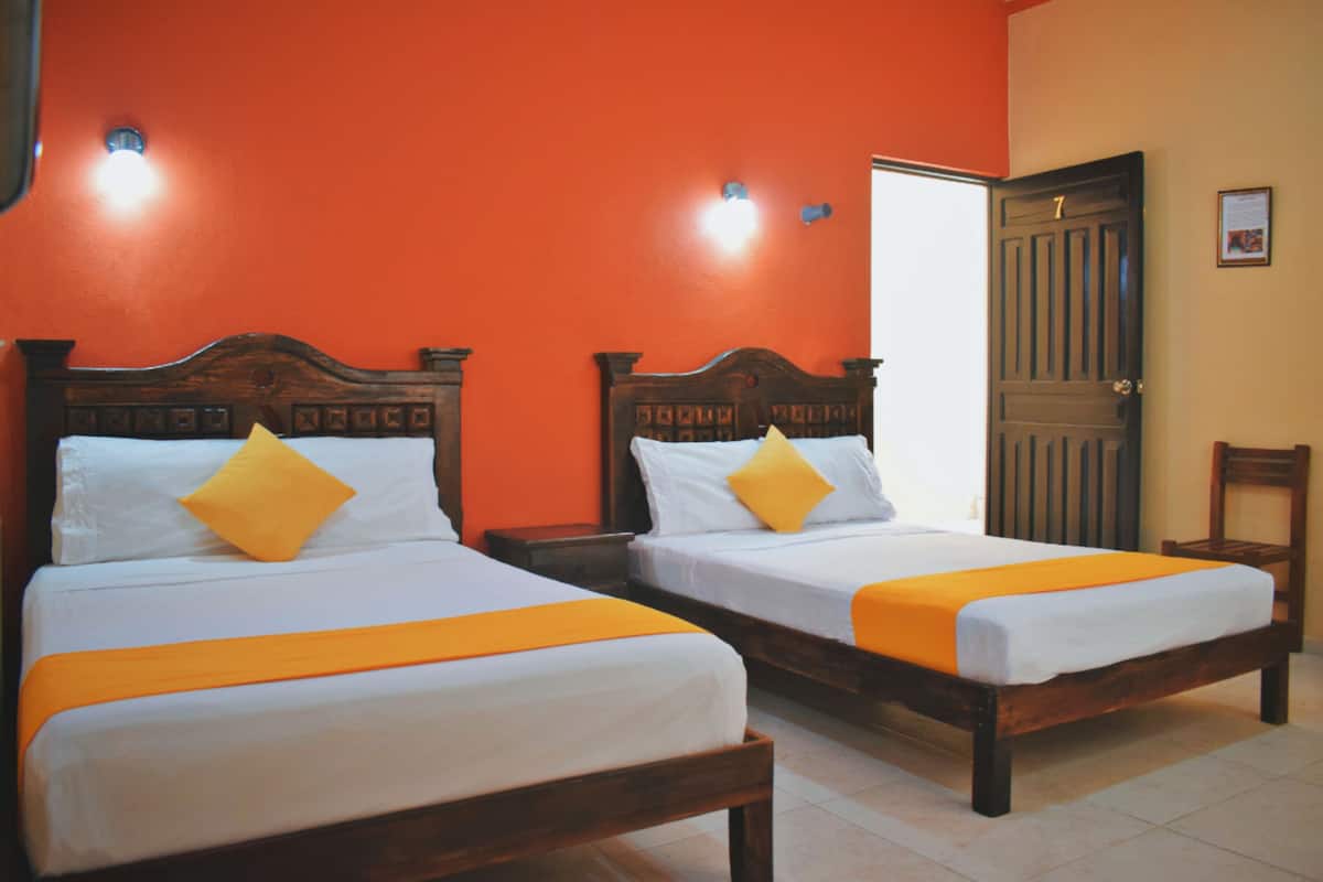 Two double beds with wooden frames and white bedding, orange bedspreads, and a bright orange wall.