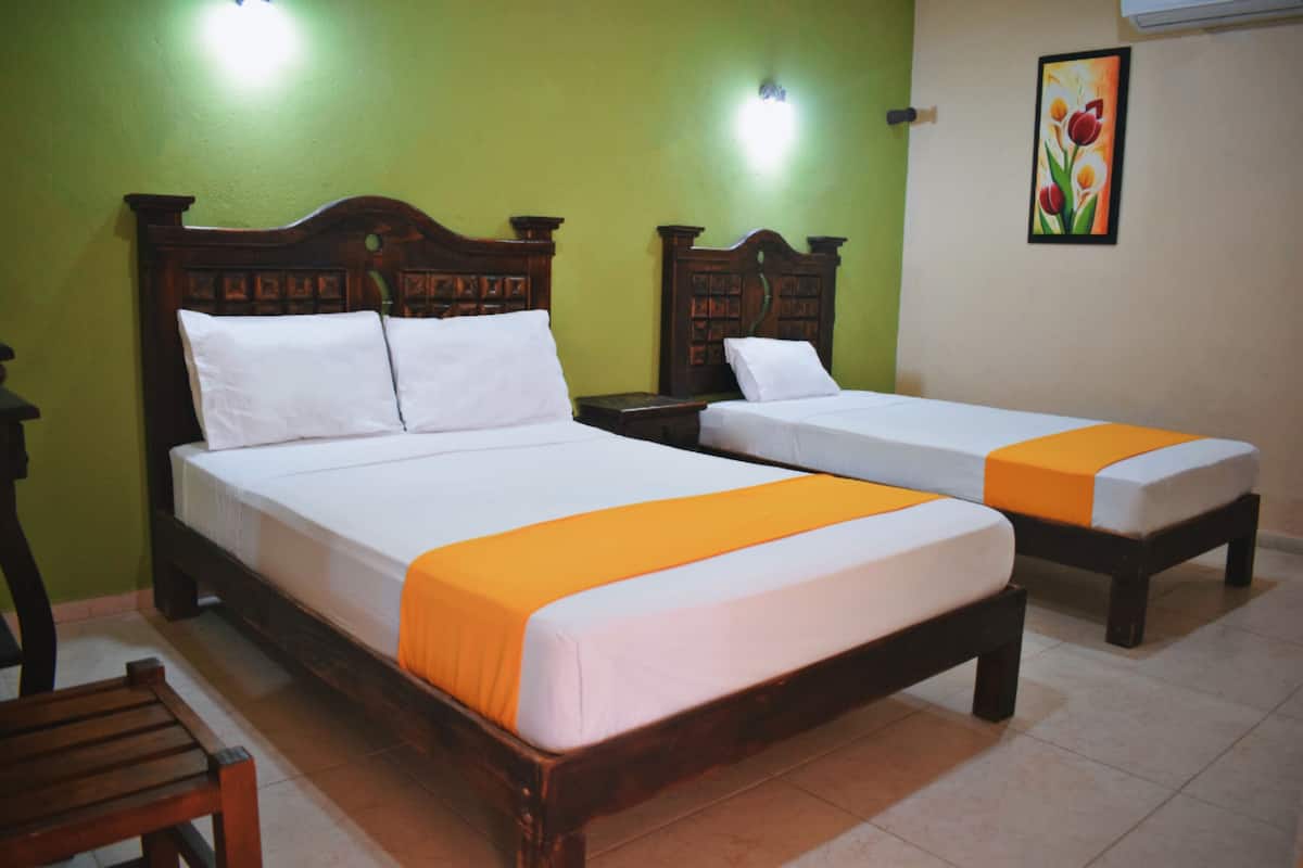 A room with two wooden beds with white linens and orange bedspreads, a wooden nightstand, and a green wall with a flower painting.