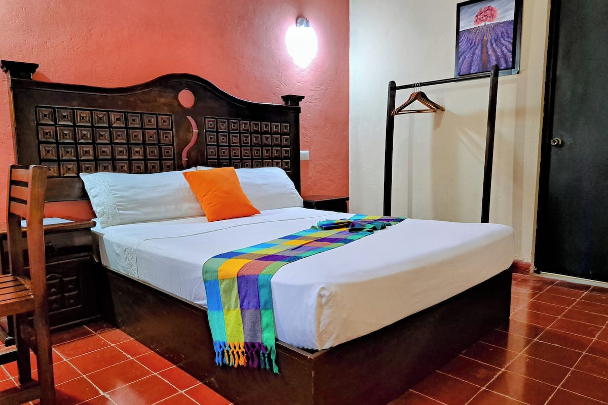 A neatly made bed with a colorful blanket, a wooden headboard, and a single orange pillow.