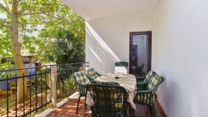 Een balkon met een tafel, stoelen, een deur en een boom.