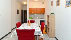 Een kleine keuken met houten kastjes, een eettafel met rode stoelen en een klein aanrecht met een plant.