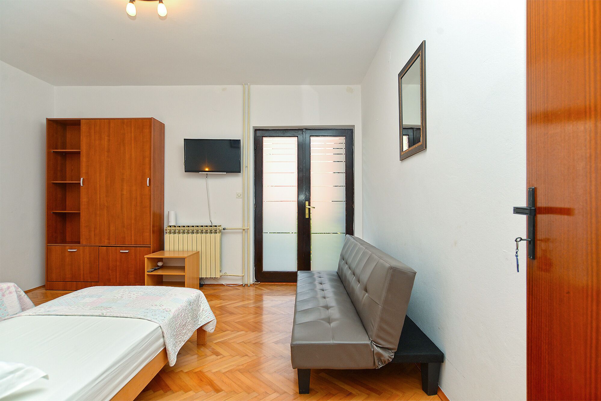 A bedroom with a bed, a bench, a wardrobe, a radiator, a television, and a door.