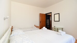 Een slaapkamer met twee eenpersoonsbedden, een houten garderobe, een klein tafeltje en een spiegel aan de muur.