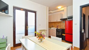 Een kleine keuken met een rode koelkast, een fornuis en een spoelbak. Er staat een eettafel met een vaas bloemen.