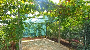 A stone-paved patio with a pergola covered by a green netting, surrounded by lush greenery. - Apartment 461/1081 (Istria - Stinjan), 900m from the beach (Stinjan)